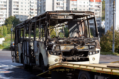 A completely burnt passenger bus is being loaded onto a tow truck.