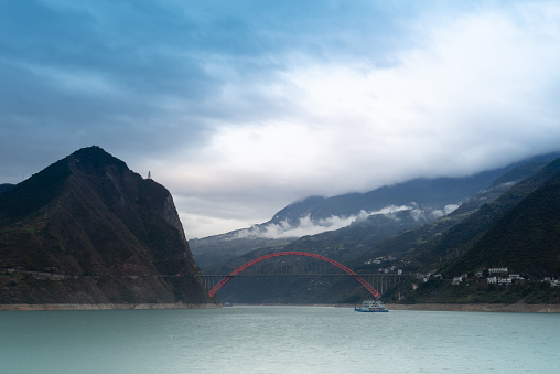 The red Wushan Yangtze River Bridge is breathtakingly beautiful, gracefully spanning the river against a backdrop of cloud-covered mountains.