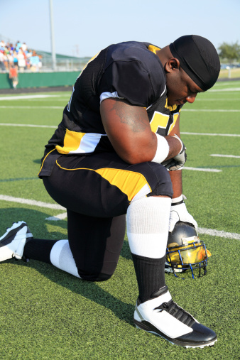 A football player gets down on one knee and says a prayer before the big game.
