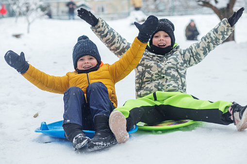 Children ride on snow plate and having fun. Outdoor play. Cold temperature. Winter time.