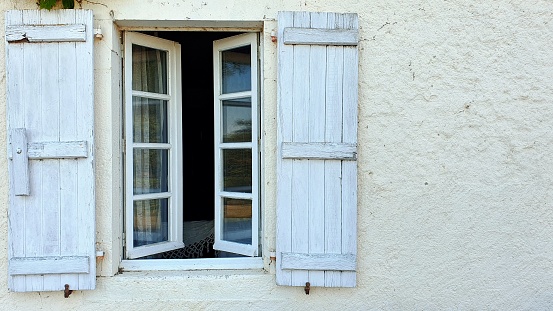Old wooden shutters worn by the passage of time. The windows reflect the exterior of the house and the interior shows a bed.