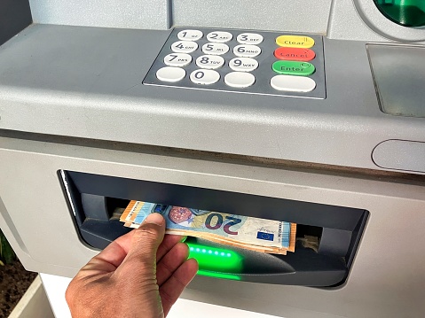 A man's hand takes out money from an ATM such as 10 and 20 euro bills to buy products