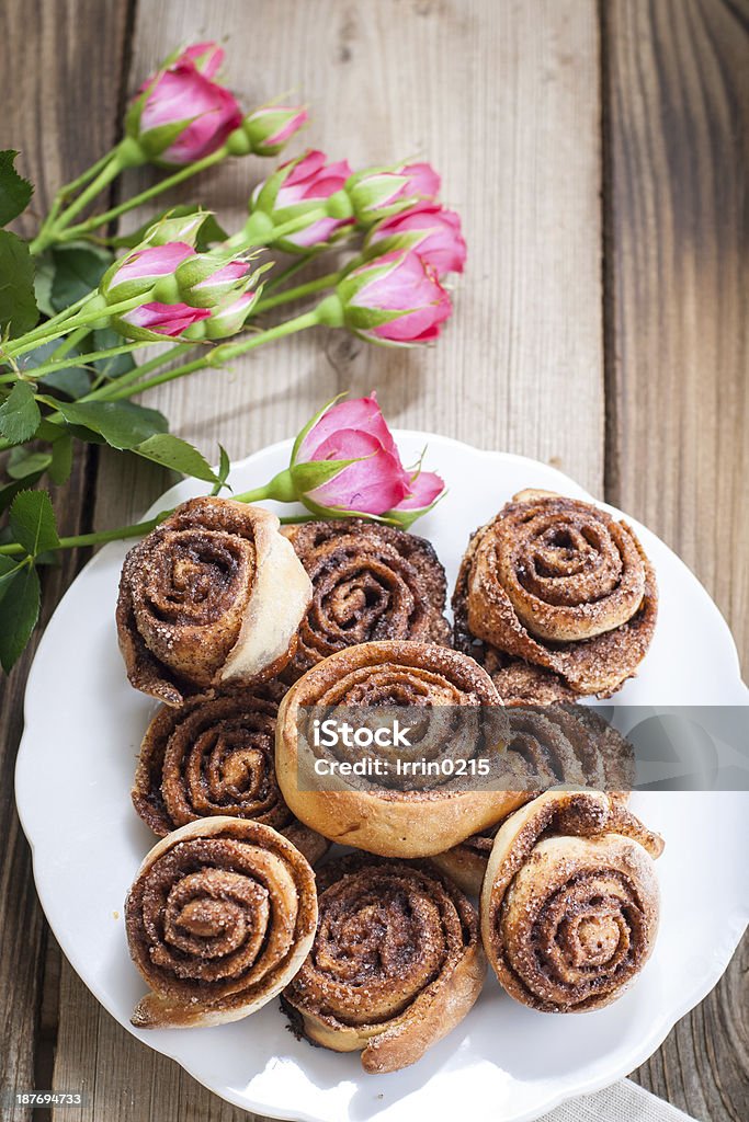 Cinnamon rolls Cinnamon buns and pink roses on a wooden background Backgrounds Stock Photo