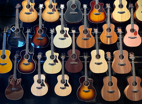 a wall full of acoustic guitars of different models and types of wood, guitars store, guitars hanging in a wall, horizontal