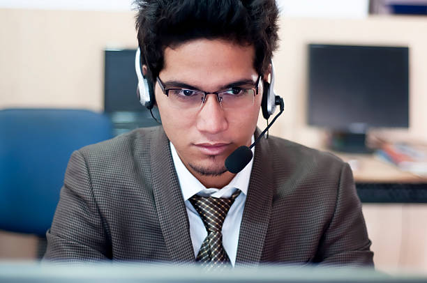A businessman on a headset taking a call Young customer service operator talking on headset and using computer in an office. sri lanka business stock pictures, royalty-free photos & images