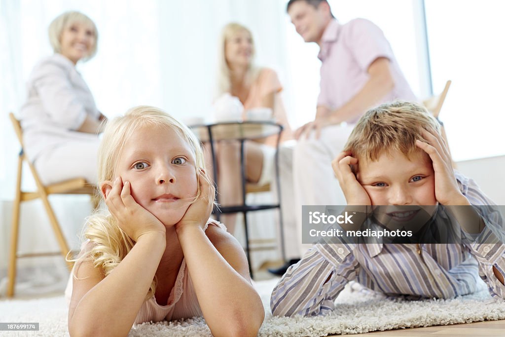 Amusing kids Funny little sibling lying on the floor, their parents and grandmother in the background 6-7 Years Stock Photo