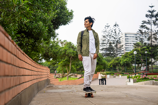 Mid-shot full body view of young Hispanic man skateboarding on Miraflores Boardwalk, Peru