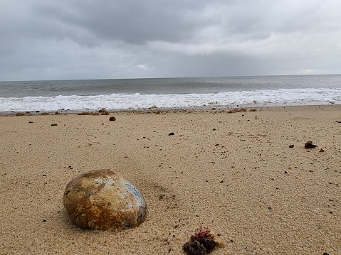 A focus on a pebble on a sandy beach with stormy clouds.