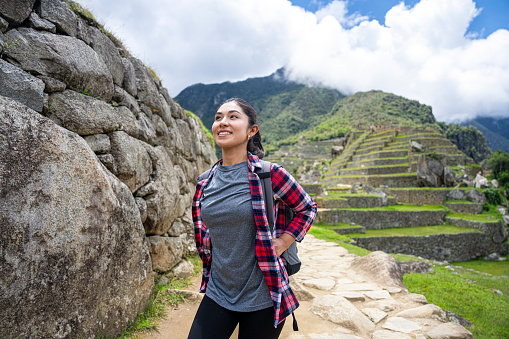 Mid-shot front view of young Latin woman enjoying the view while standing on footpath in Sacred City of Machu Picchu, Peru