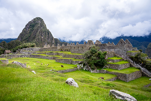 Machu Picchu illuminated by the warm sunset light. Wide angle view from the terraces above with scenic sky and sun burst. Dreamlike travel destination, world wonder. Cusco Region, Peru.