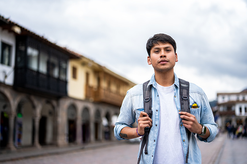 Mid-shot front view of young Latin American manlooking at camera while sightseeing in Plaza Mayor, Cusco, Perú