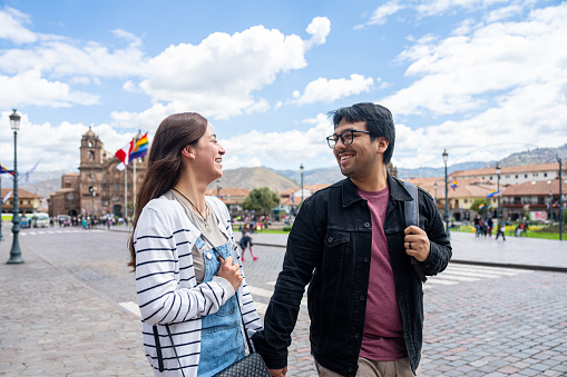 Mid-shot front view of cheerful young Hispanic couple taking a walk while sightseeing in Plaza Mayor, Cusco, Perú