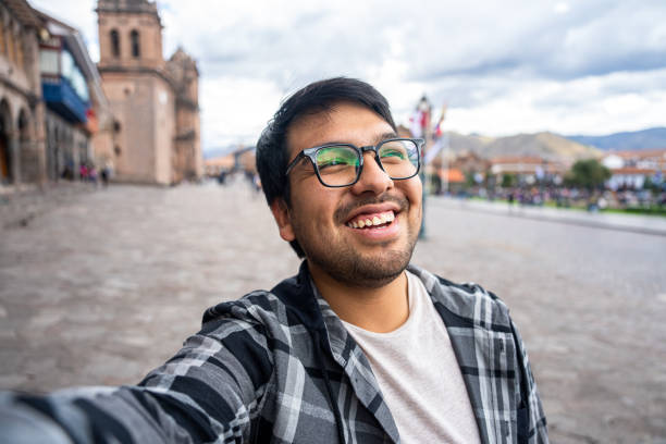 istock Front view of young Latin man taking a selfie while sightseeing Plaza Mayor, Cusco, Peru 1877058173