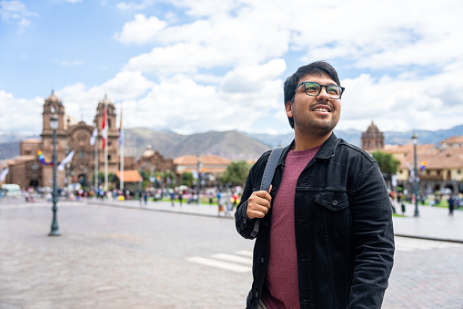 Medium shot front view of young Hispanic man taking a walk while  enjoying the sights in Plaza Mayor, Cusco, Perú