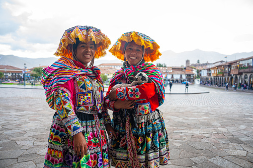 Mid-shot front view of two indigenous Peruvian women looking at camera while standing in Plaza Mayor, Cusco, Perú