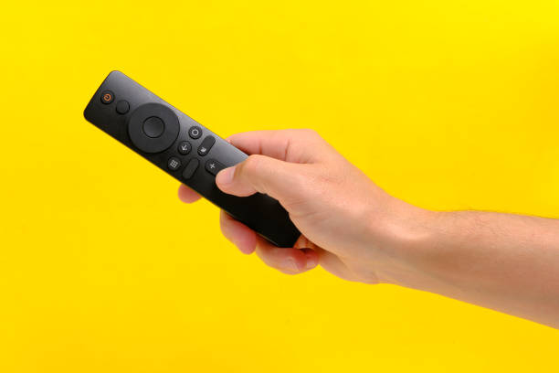 istock Hand yellow background holds TV remote by pressing button with finger. 1877067132