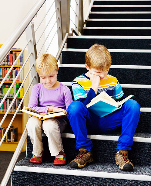 istock Two blond baby bookworms enjoy reading on library steps 187709436