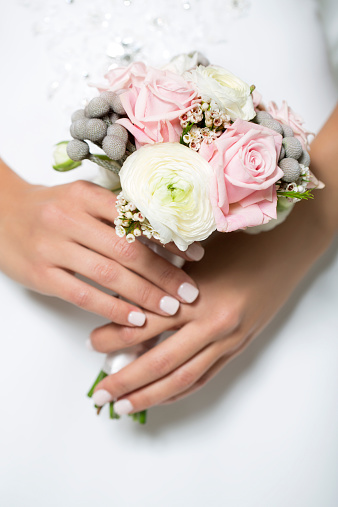 Studio shot of young beautiful bride holding a bouquet on light background