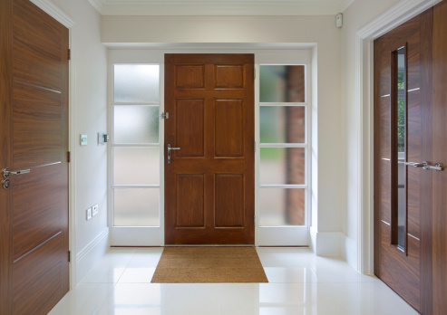 a front door of a new house with a high quality large oak panelled front door set in a white frame with opaque glass windows on either side. To the left is a door to a cloak cupboard and to the right is a glass panelled door to a reception room.