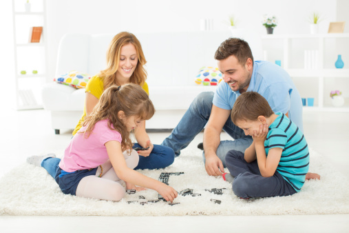 Young Cheerful Family with two children having fun together at home, playing domino.