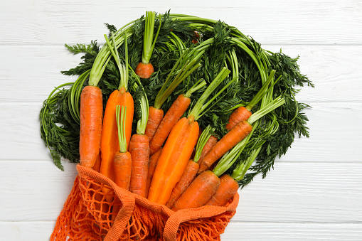 Carrots, celery and parsley in a paper grocery bag on a rustic old wood tabletop