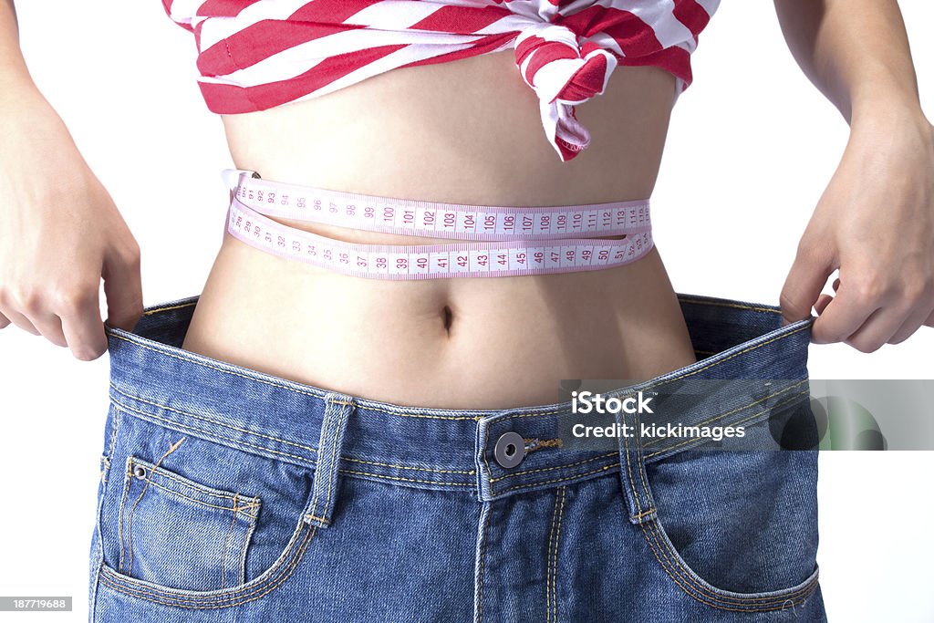 Woman with Measuring Tape Wearing Loose Jeans Close-up of woman's waist with measuring wearing loose jeans. Abdomen Stock Photo
