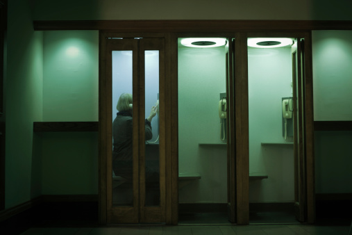 Woman using a phone inside a phone booth in a dark hallway.