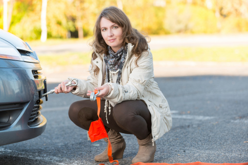 Beautiful woman assembling towing hook to a broken car and holding tow rope in the other hand