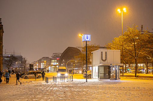 Steintorplatz, Hamburg, Germany - December 5th 2023:  People walking in the snow in front of an elevator to s subway station on a cold late winters evening