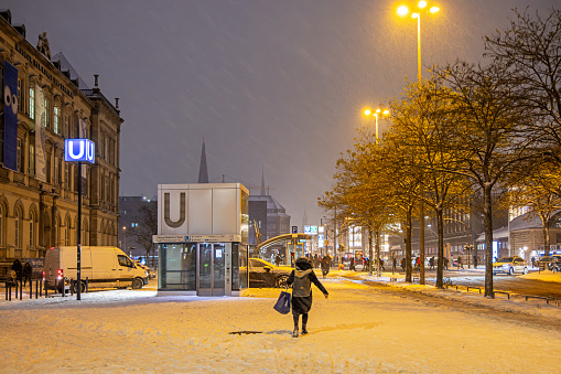 Steintorplatz, Hamburg, Germany - December 5th 2023:  People walking in the snow in front of an elevator to s subway station on a cold late winters evening