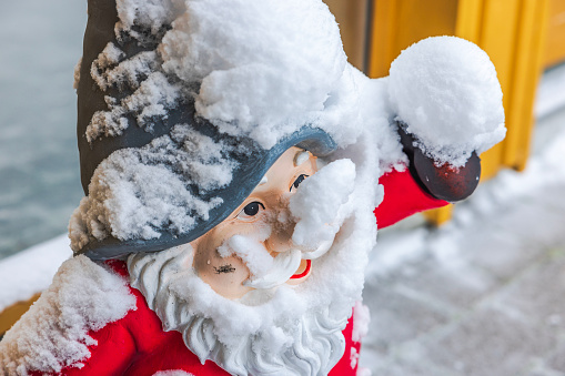 Close-up view of snow-covered gnome's face standing outside near entrance to house.