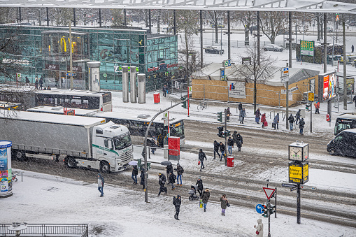 Steintorplatz, Hamburg, Germany - December 5th 2023:  People crossing a busy street with heavy traffic on a snowy day