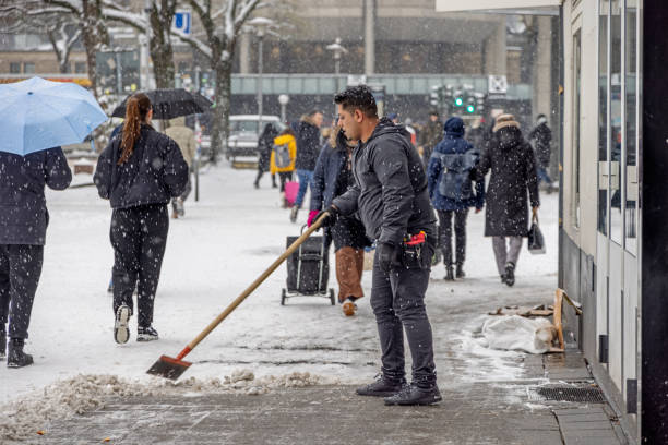 Steintorplatz, Hamburg, Germany - December 5th 2023:  Man clearing the snow on the sidewalk between the pedestrians on a snowy winters day