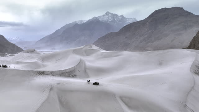Scenic aerial view drone view flying over sand dunes Sarfaranga Cold Desert, Surrounding with Snow Cap Mountain in Skardu, Northern Pakistan