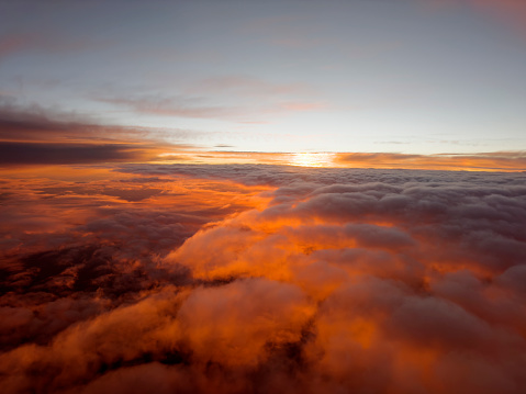 A view from an passenger jet plane of a sunrise that is breaking through the clouds bathing them in golden light