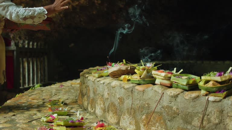 Balinese woman performs a ceremony of offerings to Hindu God. Smoke of aroma incense. Burning sticks. Indonesian culture in Bali.