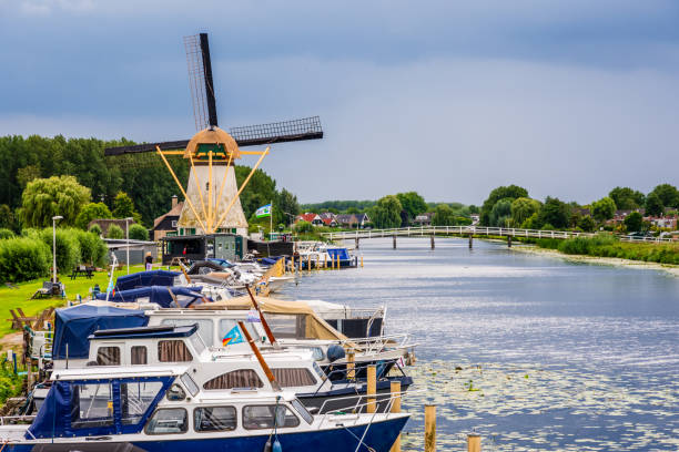 Alblasserdam, Netherlands - July 29, 2023: The Kortlandse windmill, built in 1890, with riverboats moored along the canal and the Witte Brug footbridge on a stormy summer afternoon.