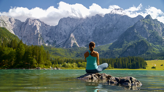 Amidst the Serenity of Nature,a Female Tourist Sits on a Rock,Gazing at the Majestic Rocky Mountains. The Scene Unfolds by a Lake,Portraying a Tranquil Moment of Contemplation and Admiration for the Breathtaking Beauty of the Surrounding Landscape