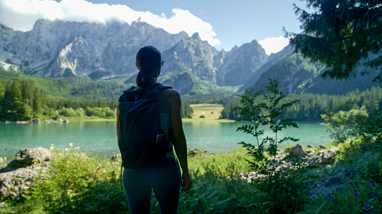 In the Embrace of Summer,a Rear View Captures a Female Tourist With a Backpack,Gazing at the Majestic Rocky Mountains and an Idyllic Lake. The Scene Reflects the Spirit of Adventure and the Breathtaking Landscapes that Define a Memorable Summer Journey