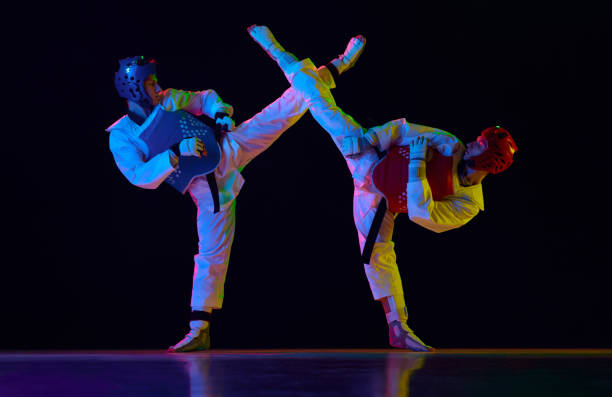 istock Athletic, strong young men, taekwondo athletes in motion, fighting, training against black background in neon light. Martial arts, combat sport 1877373621