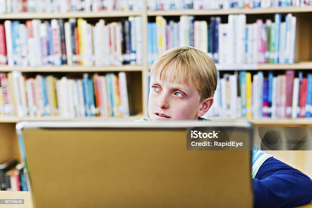 Capelli biondi Scolaro elementare con portatile in biblioteca si distrae - Foto stock royalty-free di 10-11 anni