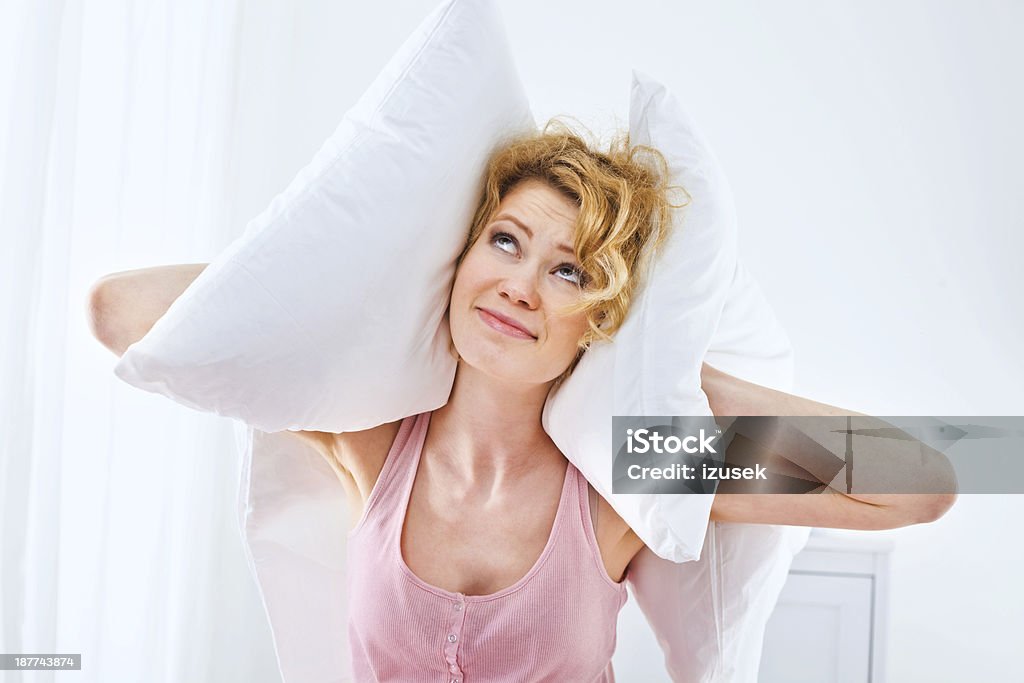 Rude neighbors Unhappy young adult woman squeezes pillows to her ears, can't sleep because of a big noise. Hands Covering Ears Stock Photo