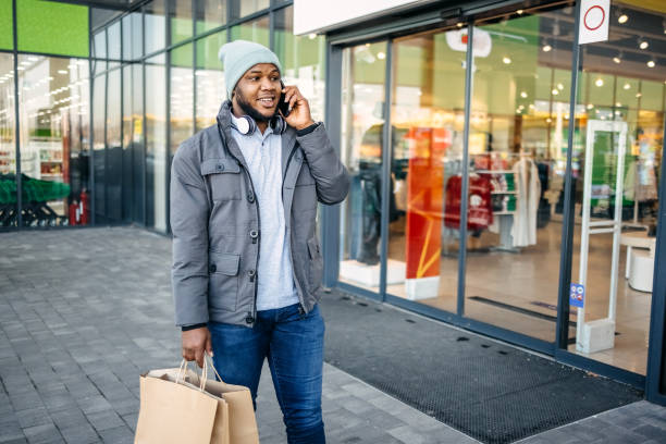 istock Young black man carrying bags in shopping centre while talking on mobile phone 1877481641