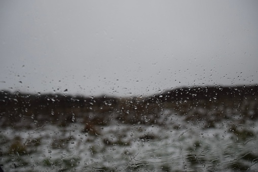 A snowy field and sky through a wet window.