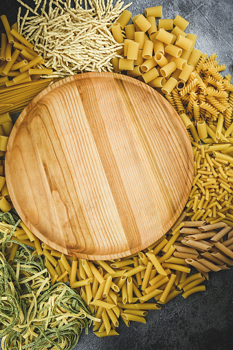 Wooden board with Italian raw pasta around.