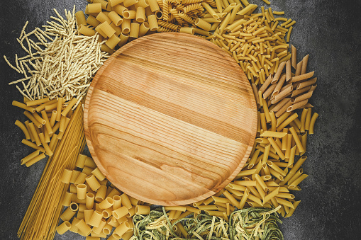 Various mix of pasta with empty wooden plate in center.