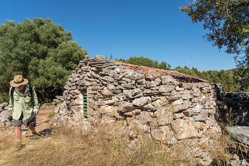 Man hiking in Telascica, national park in Dugi otok island, small old stone stable for sheep or goats. Croatia