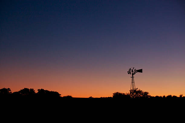 Silhouette of an old farm windmill at dusk stock photo