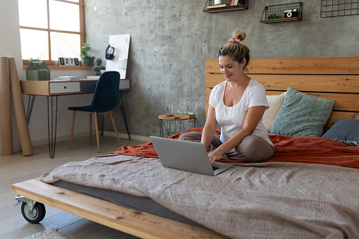 Woman using laptop while sitting in bed at home.