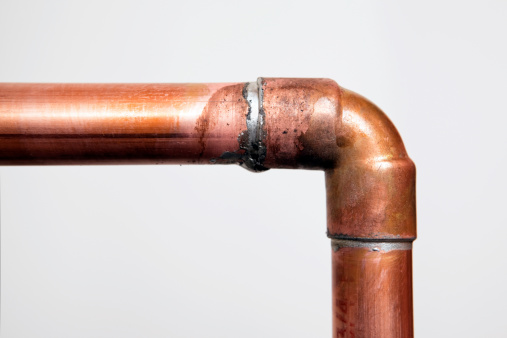 Two copper water pipes joined with a 45 degree elbow. The solder has been applied by sweating, which is, heating the pipe with a torch and touching the solder to the joint, the molten metal is drawn into the joint. The background is gray drywall.